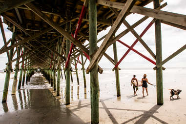 people walking a dog beneath a boardwalk in folly beach