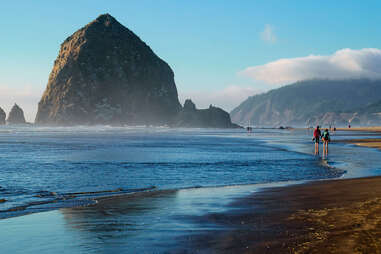 people walking along the beach near a giant rock